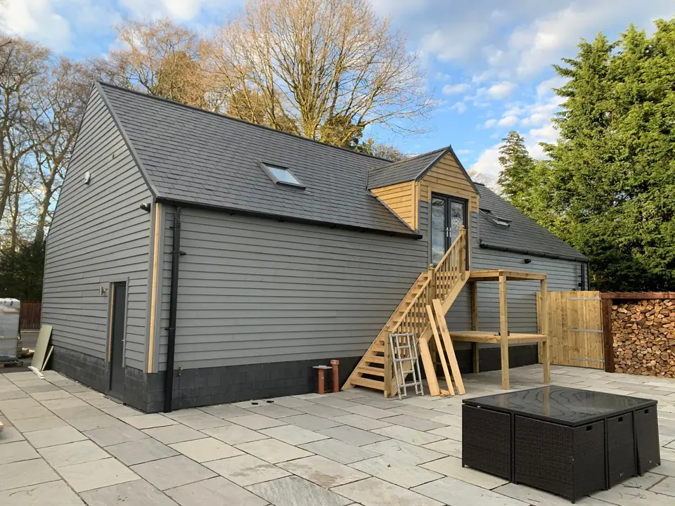 Grey-clad barn building with an external timber staircase and a paved terrace