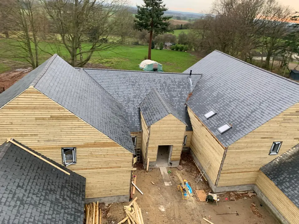 Aerial view of a group of timber-framed barn buildings with slate roofs, still in bare timber boarding