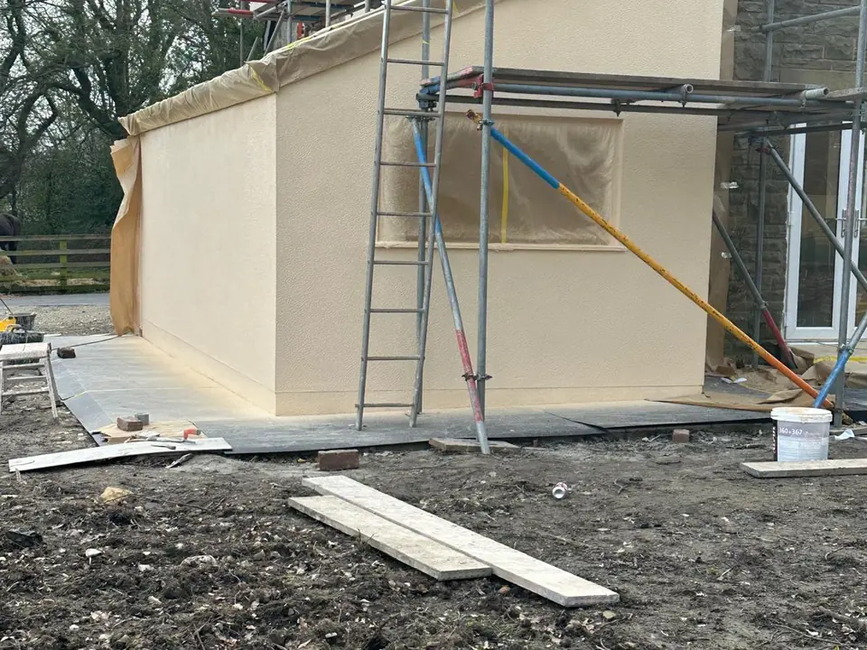 The same extension finished in a smooth cream render, with the scaffolding still against the main house