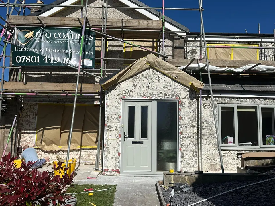 Front of a semi-detached house under scaffolding, with its old textured wall finish, the windows masked up and an Eco Coatings banner on the scaffold